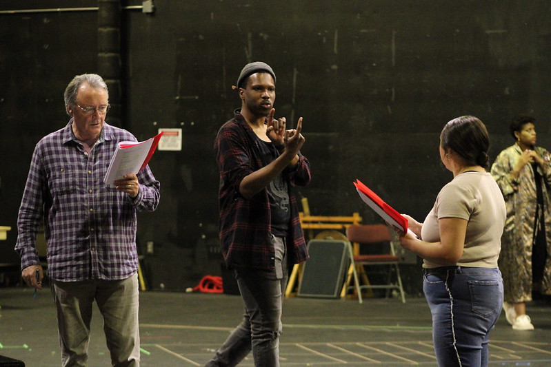Corey Allen gives blocking to two actors, using his hands to show how they should cross the stage
