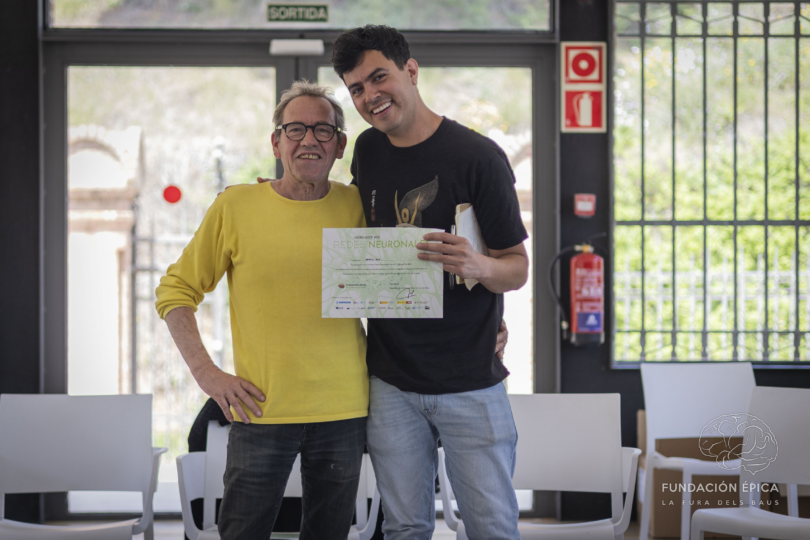 Daniel Ruiz Bustos holds a certificate after completing the Redes Neuronales workshop, posing with a founder of La Fura dels Baus