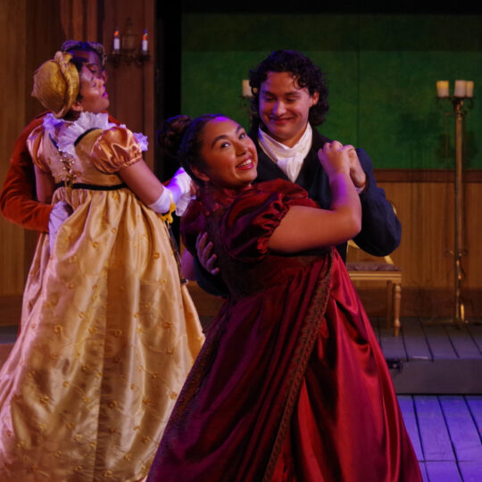 Four actors dance on stage together, wearing regal gowns and suits, with Esmeralda Treviño and Dominic Gross dancing together in the foreground