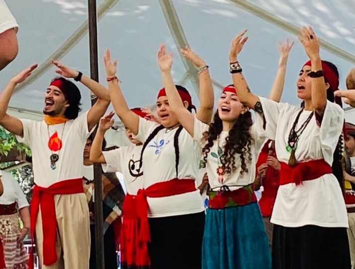 Four participants and interns at the Indigenous Arts Summer Encounter raise their arms and smile