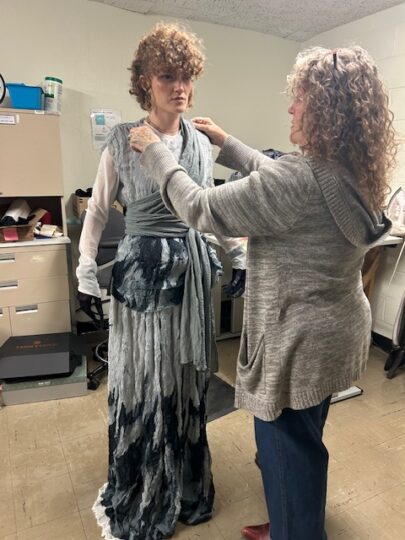 Nanette Acosta adjusts the collar of a costume piece that Kira Small is wearing