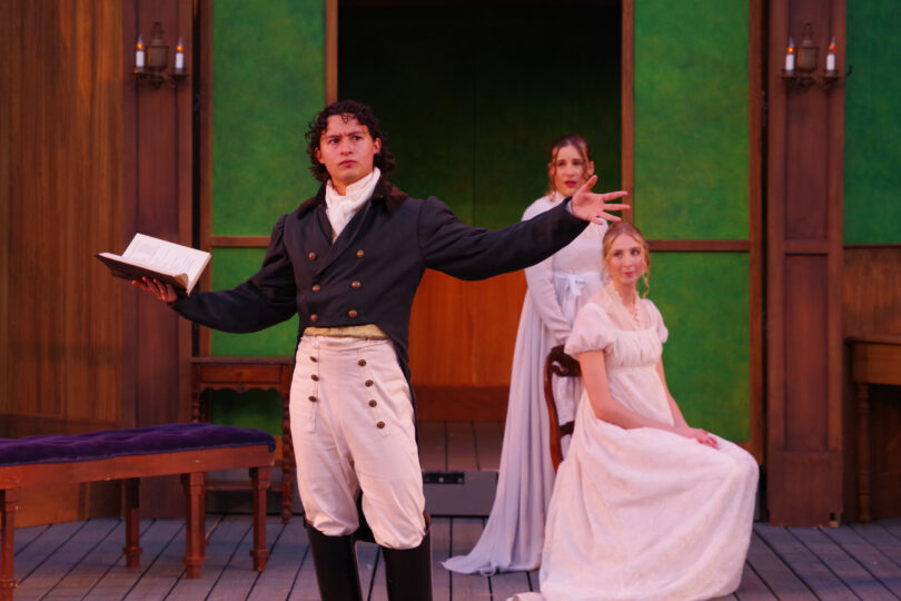 Three actors perform a scene from SENSE AND SENSIBILITY, including Dominic Gross, who holds his out wide while reading from a book