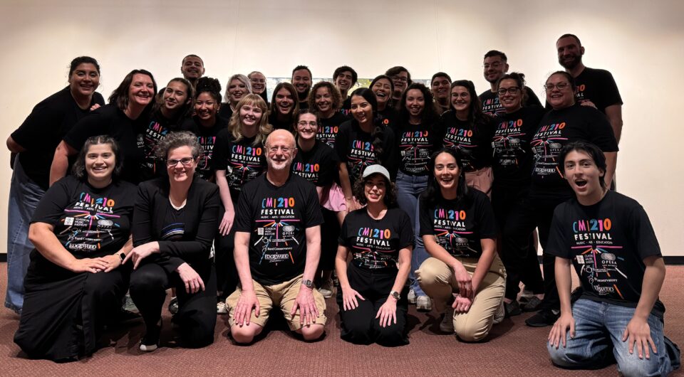 A large group of people pose together wearing black CMI 210 Festival t-shirts