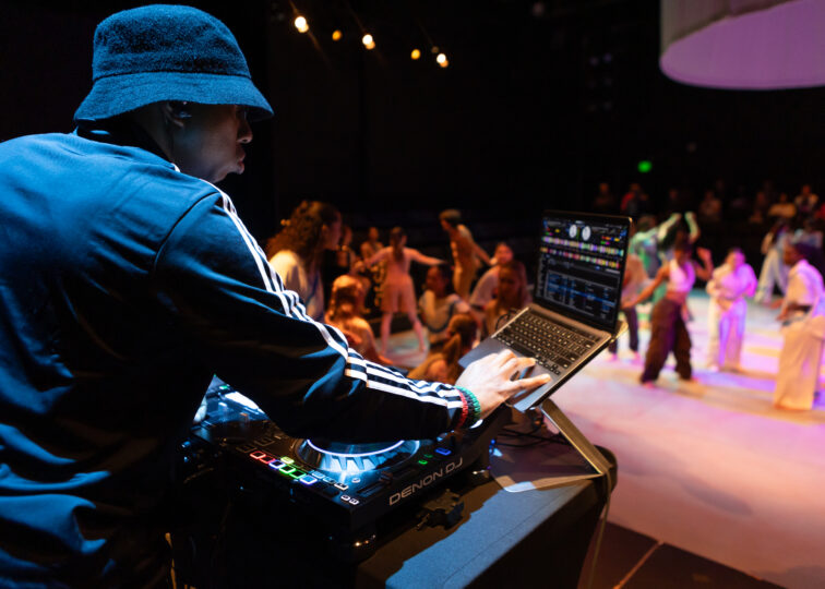 The DJ, Earnest Mazique, stands in the corner while we see the dancers on the stage over his shoulder.