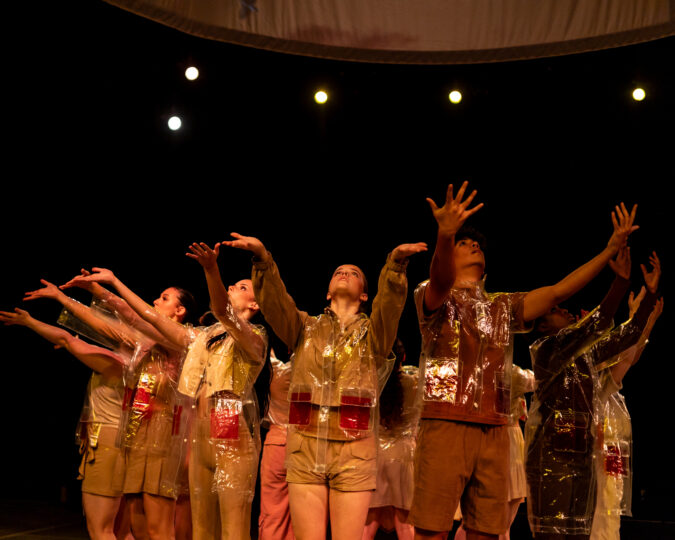 The dancers stand in a circle, facing the audience with their arms outstretched.