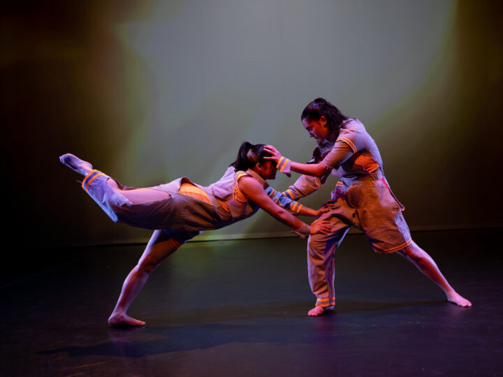 Two dancers perform, creating a sense of tension as they simultaneously lean in and push each other away