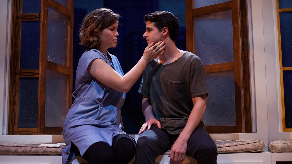 a woman and man sit on a windowsill as she holds her hand to his face