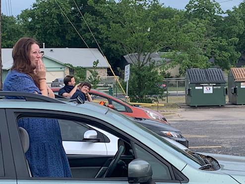 students waving through their car windows