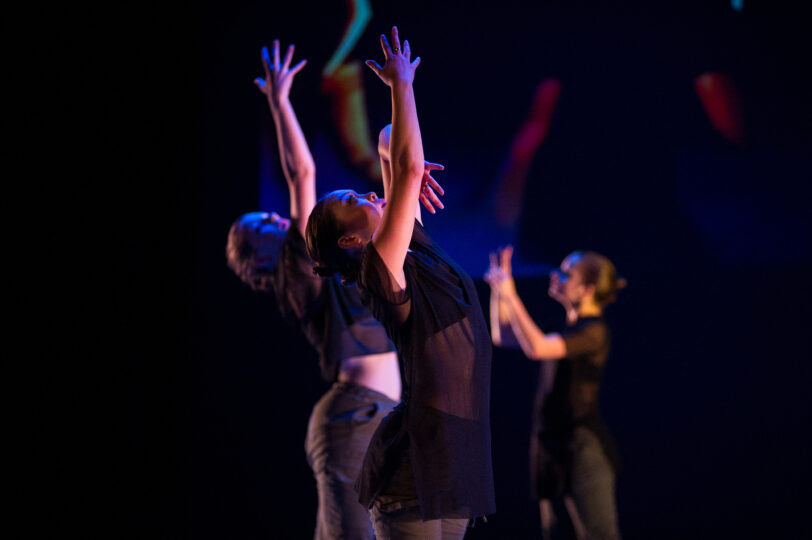 two dances pose with their right arms stretched upward and their left hand meeting their right elbow, looking upwards
