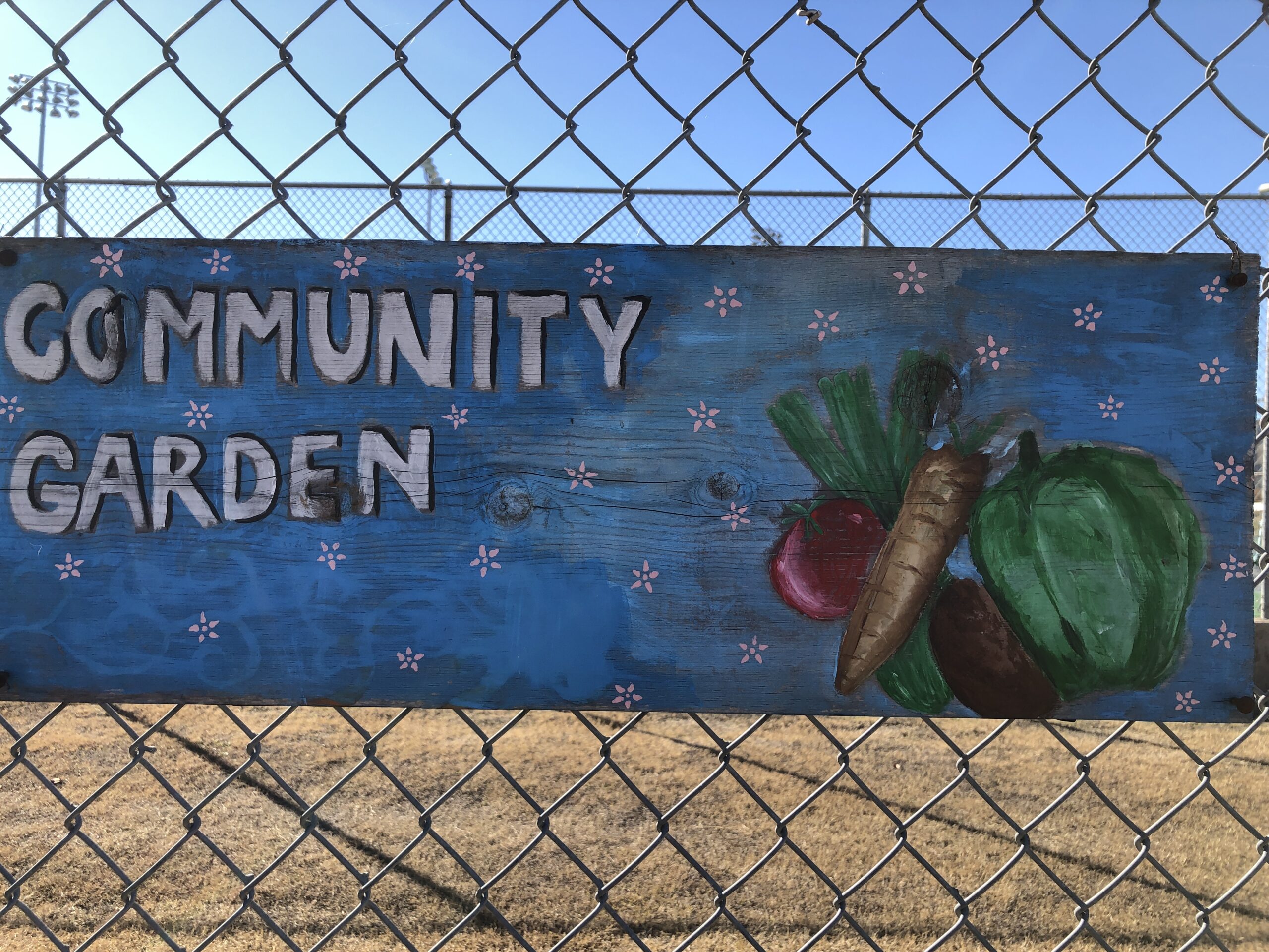 a painted wooden sign that has "Community Garden" written in white lettering and vegetables painted in the corner