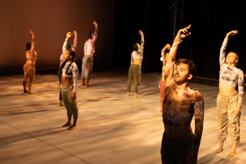 dancers stand spread out on stage with their right arms raised