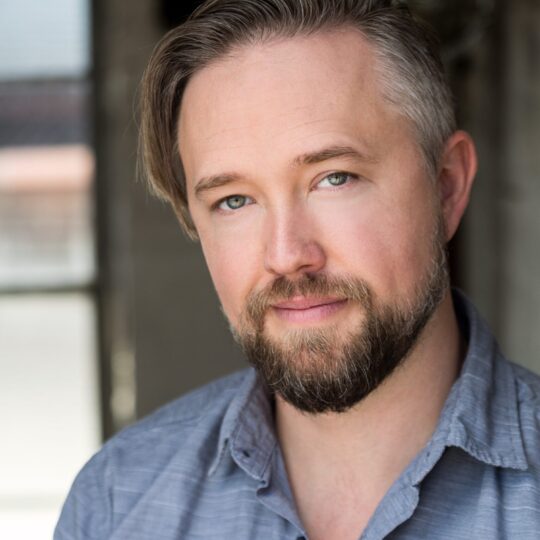 man with blonde hair and a beard wearing a blue button up