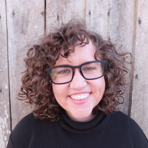 woman with short, curly hair stands in front of a wooden backdrop