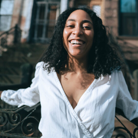 woman with black curly hair wearing a white long sleeve blouse