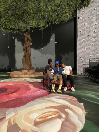 three actors sit on a bench on stage consoling one another