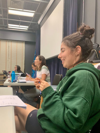 Four women look towards the cast from behind tables. They are laughing.