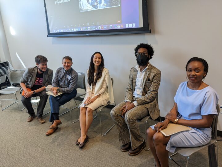 five PPP alumni sit in chairs before a panel discussion, with additional alumni on a Zoom screen behind them