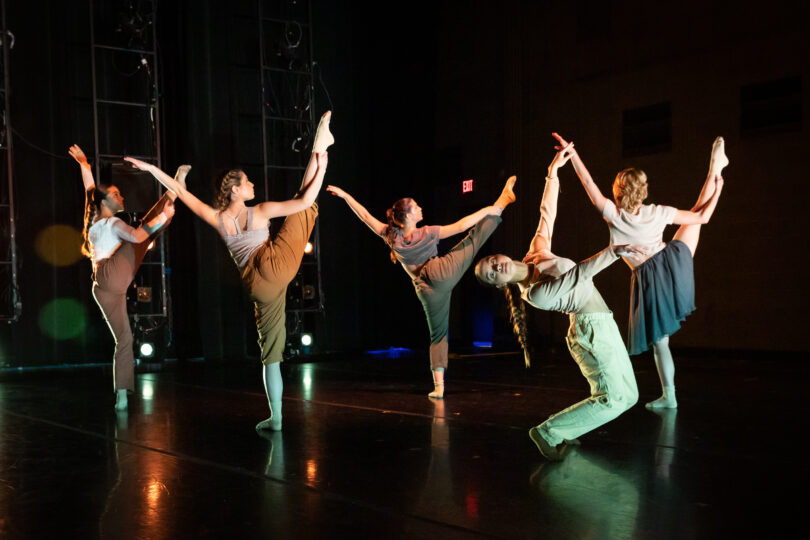 Ballet dancers wearing minimalist earth tones hold one leg in the air in a classical pose