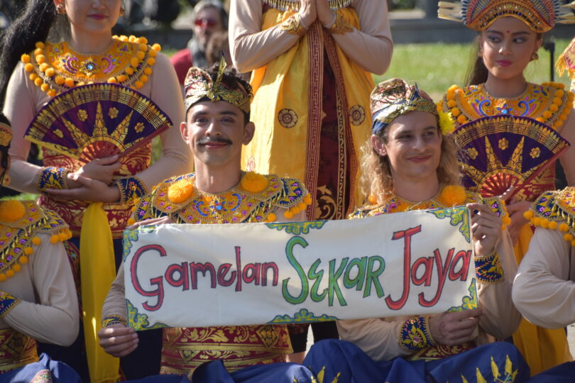Ph.D. candidate Jeffrey Gan in an intricate costume sitting with an ensemble of dancers and holding a sign reading Gamelan Sekar Jaya