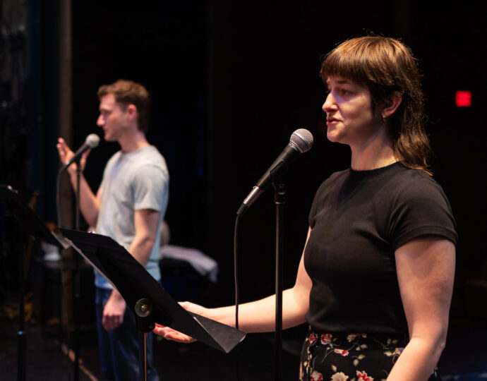 Photo of two performers speaking into microphones in the reading of Godfriend