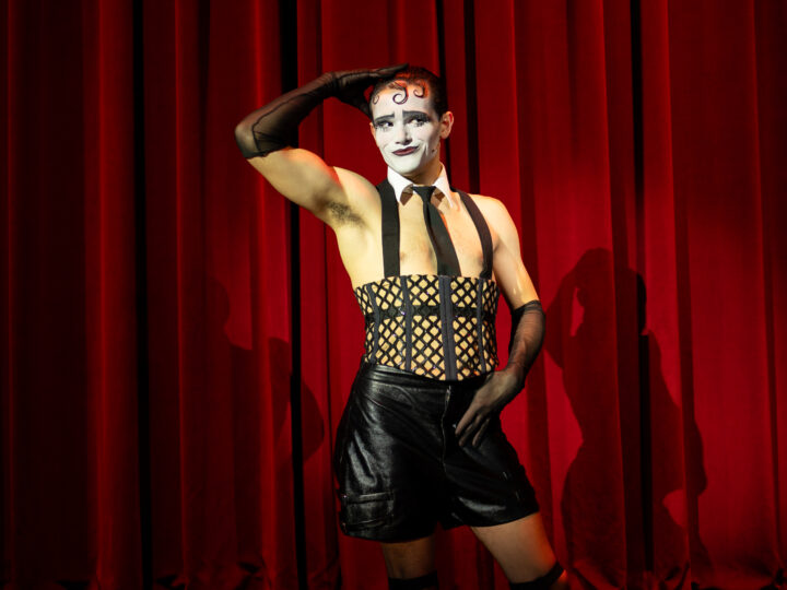David Gonima as the emcee in black leather shorts and clownish white and black makeup 