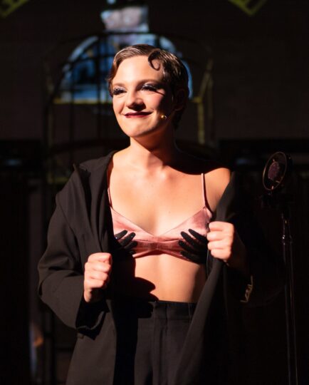 Ella Eavenson as Sally Bowles in a silk bra and black suit 