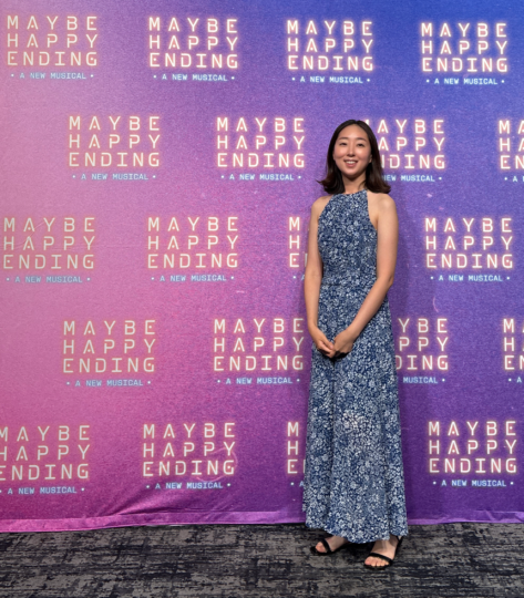 photo of a woman in a long blue and white patterned dress smiling in front of a maybe happy ending photowall