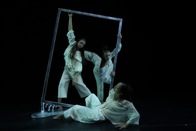Three dancers pose around a metal frame that appears as if it is melting