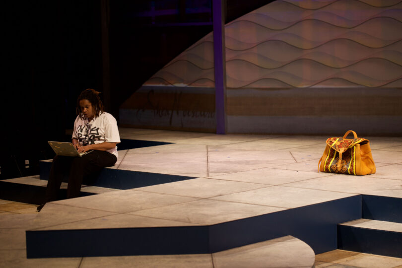 Director Mikala Gibson sits on stage near Miss Bag