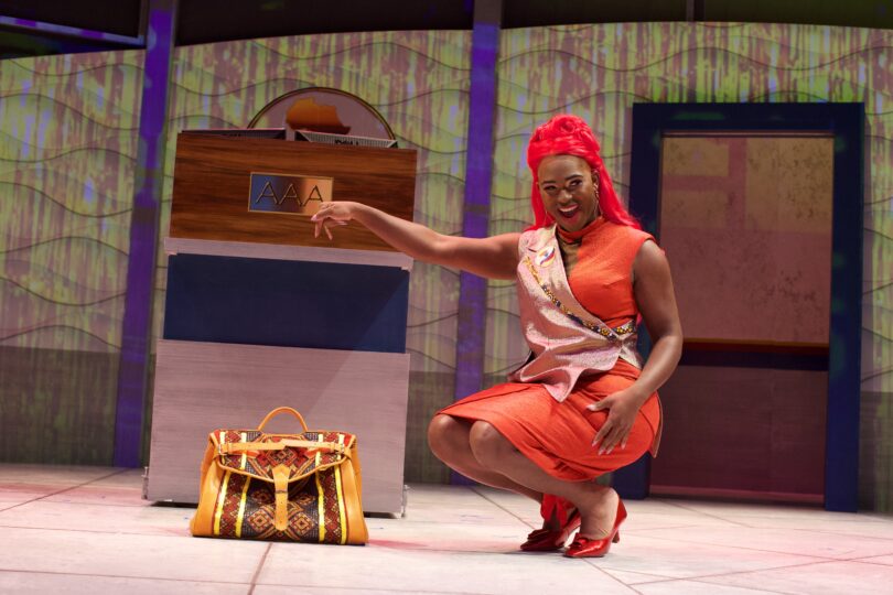 Actor Chandler Collins, portraying Peaches, points down at the prop Miss Bag