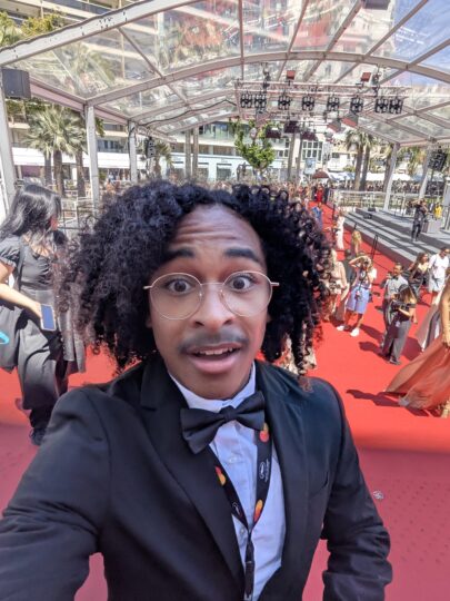 photo of man looking surprised in a tuxedo with red carpet of cannes festival photographers behind him