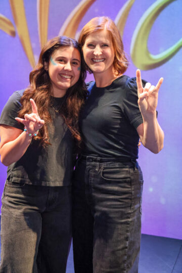 photo of two smiling women leaning into each other with hook em horns hand gestures