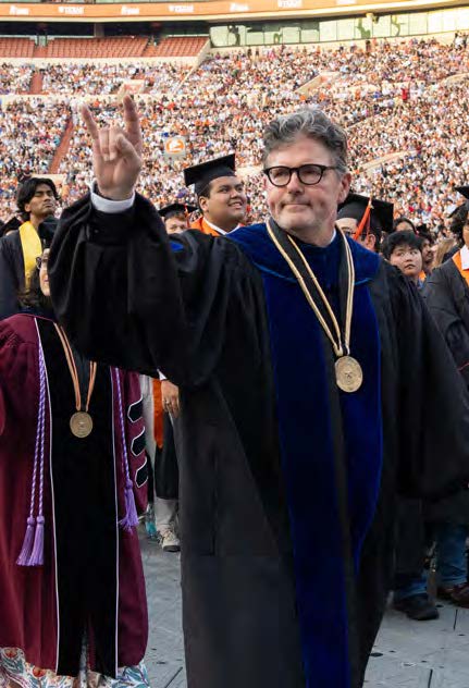 Dean Cole with the Hook Em hand sign in commencement regalia