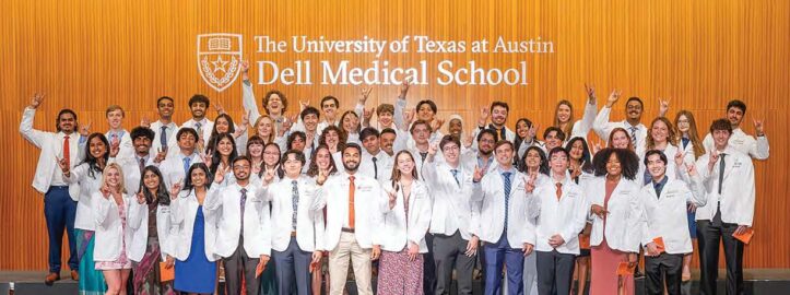 Dell Medical School students in white coats gathered for a group photo, showing Hook 'Em Horns.