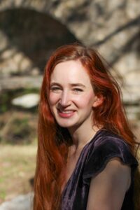 A headshot of a Caucasian woman with red hair in a purple velvet top.