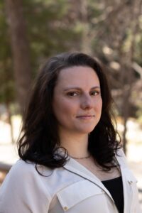 A headshot of a caucasian woman with long brown hair  in a white button down.