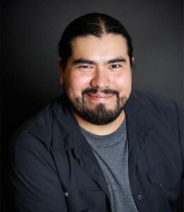 A headshot of a smiling Mexican man with a short beard and long pulled back hair.