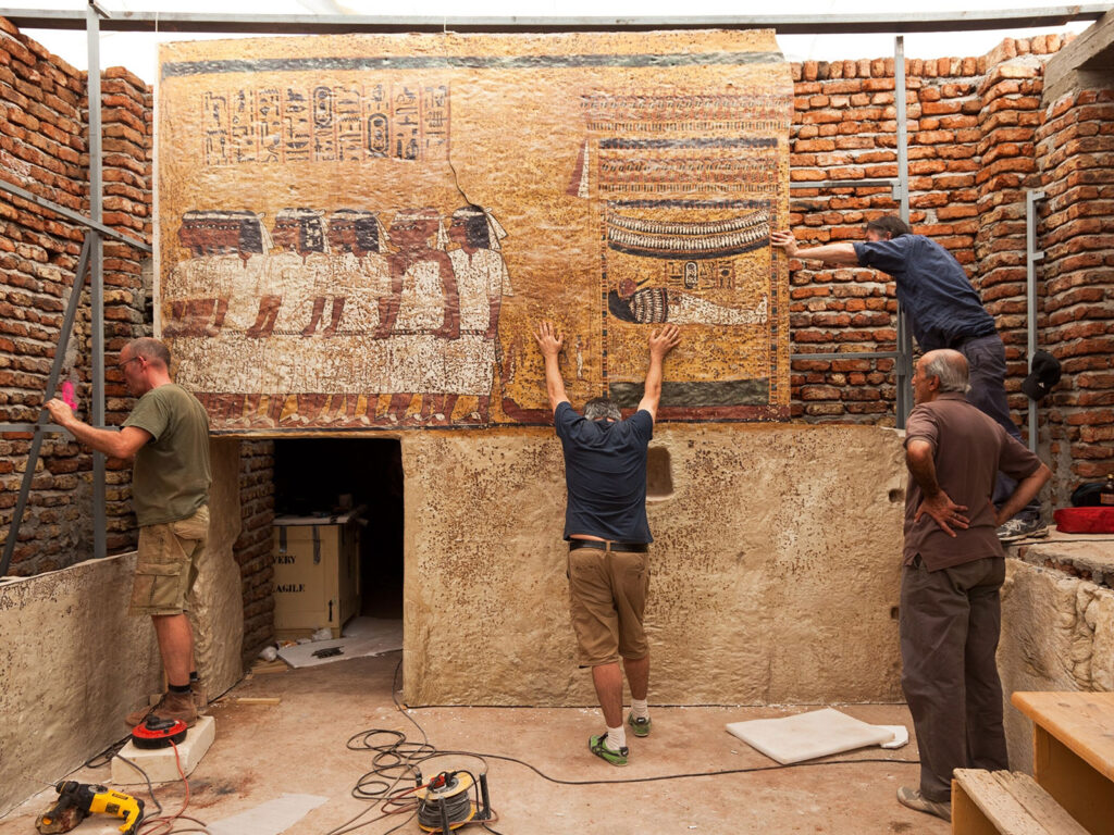 Four people working at archaeological field site interacting with wall mural