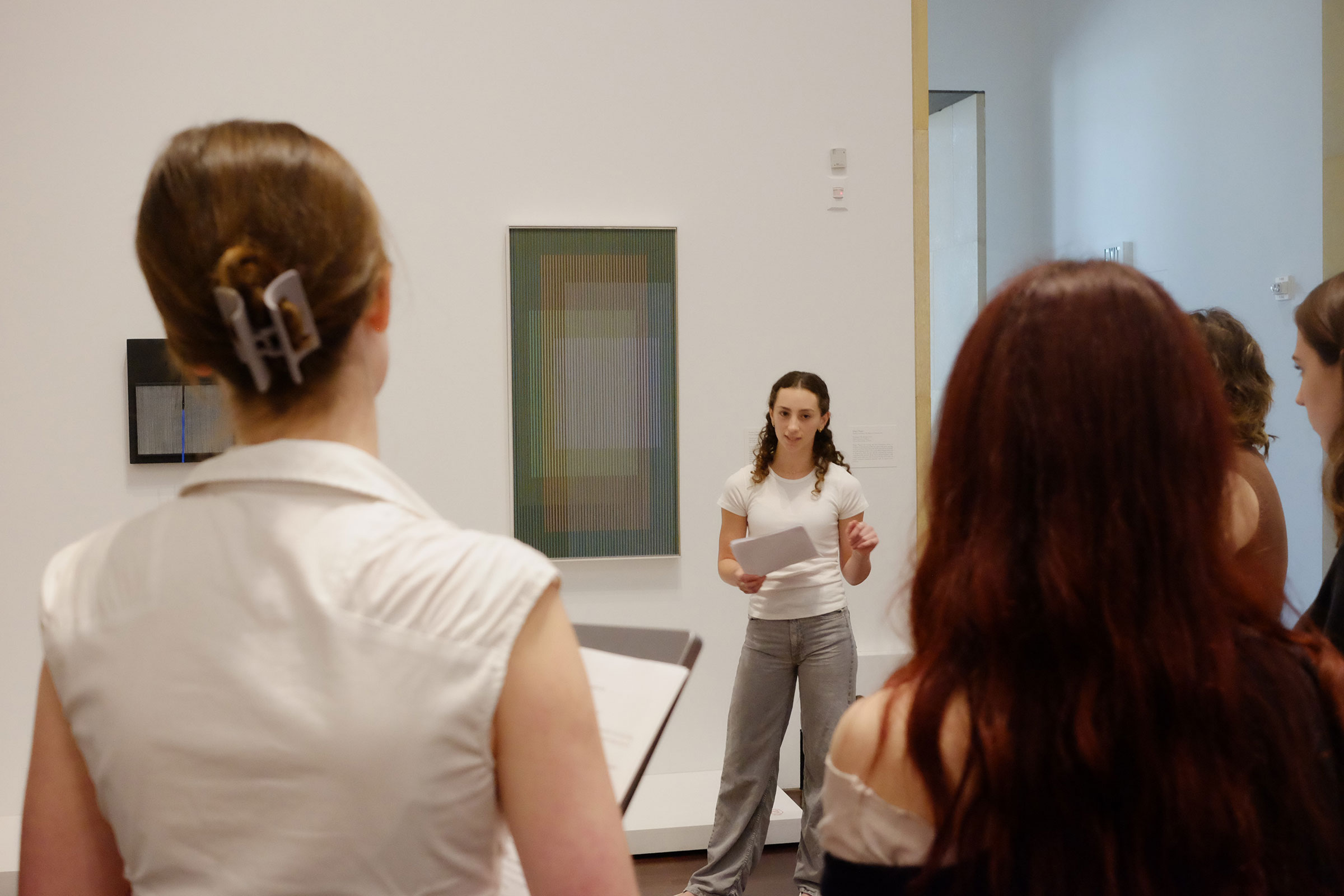 person standing next to artwork on wall and presenting to a group in the foreground