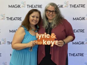 Roxanne Schroeder-Arce, Associate Dean of UTeach Fine Arts, and UT alumna Jenn Hartmann LuckLyric & the Keys in front of a step and repeat.