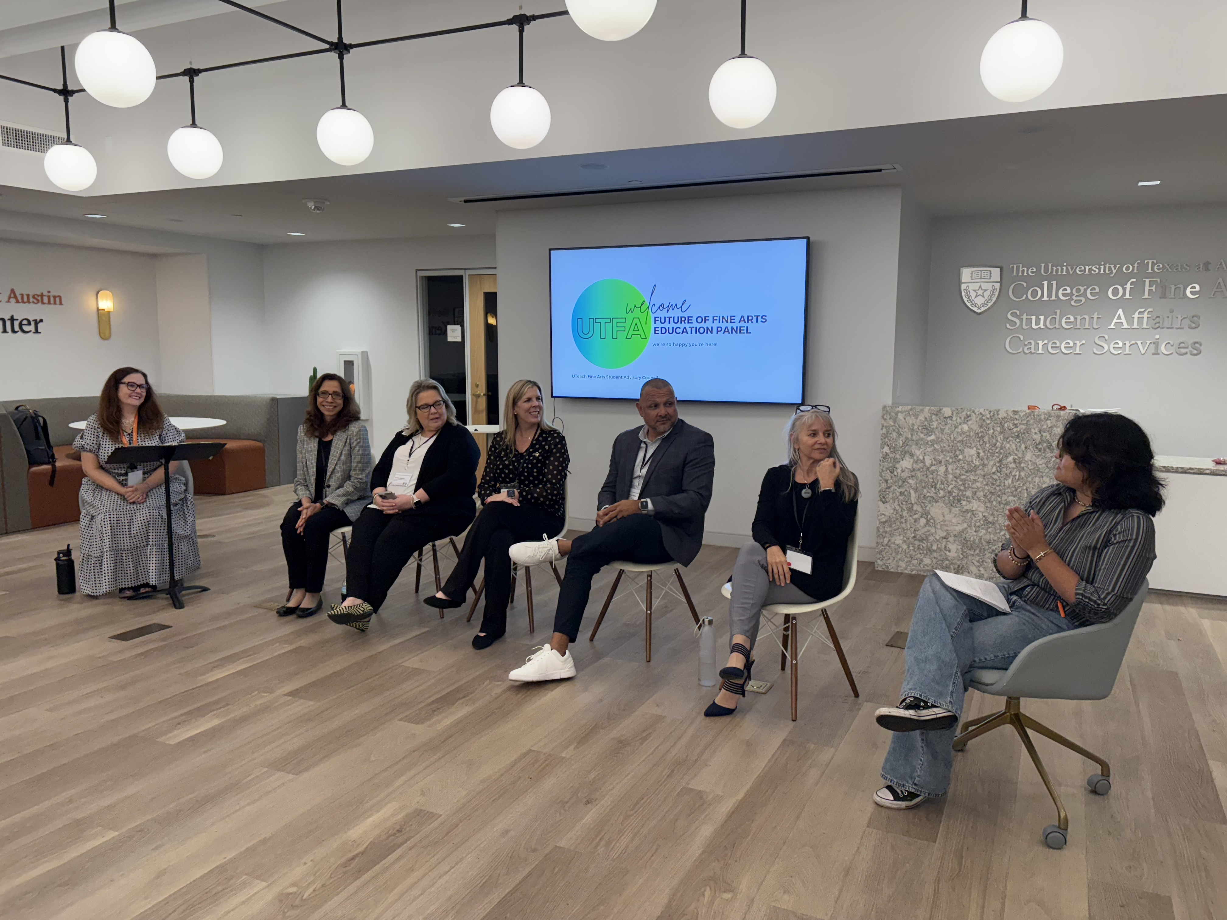 Panel guests sit in a line in the Kendra Scott Center discussing topics on Fine Arts Education. On the screen behind them is a slide that states"welcome to the Future of Fine Arts Education panel"