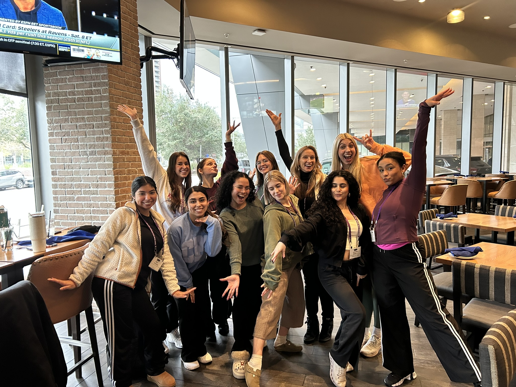 Group gathered in front of window. (L to R - back row) Sarah Johnston (Cohort 11), Claire Wood (Cohort 5), Hayley Jeansonne (Cohort 11), Dr. Tina Curran, Ashleigh Friday (Cohort 5), L to R - front row) Emily Figueroa (Cohort 11), Mia Bella Castillo (Cohort 10), Halle Hollingsworth (Cohort 9), Victoria Murillo (Cohort 5), Toni Neal (BFA Dance, Cohort 5 sibling) in different poses of arms raised.