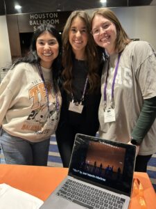 Collegiate Fair on Wednesday, January 8, 2025. Student in front of table with UTeach Fine Arts logo on tablecloth. (L to R) Emily Figueroa (Cohort 11), Sarah Johnston (Cohort 11), Hayley Jeansonne (Cohort 11).