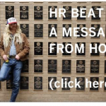 Man in wig with trucker hat standing against a wall with the text HR Beats a message from HOP